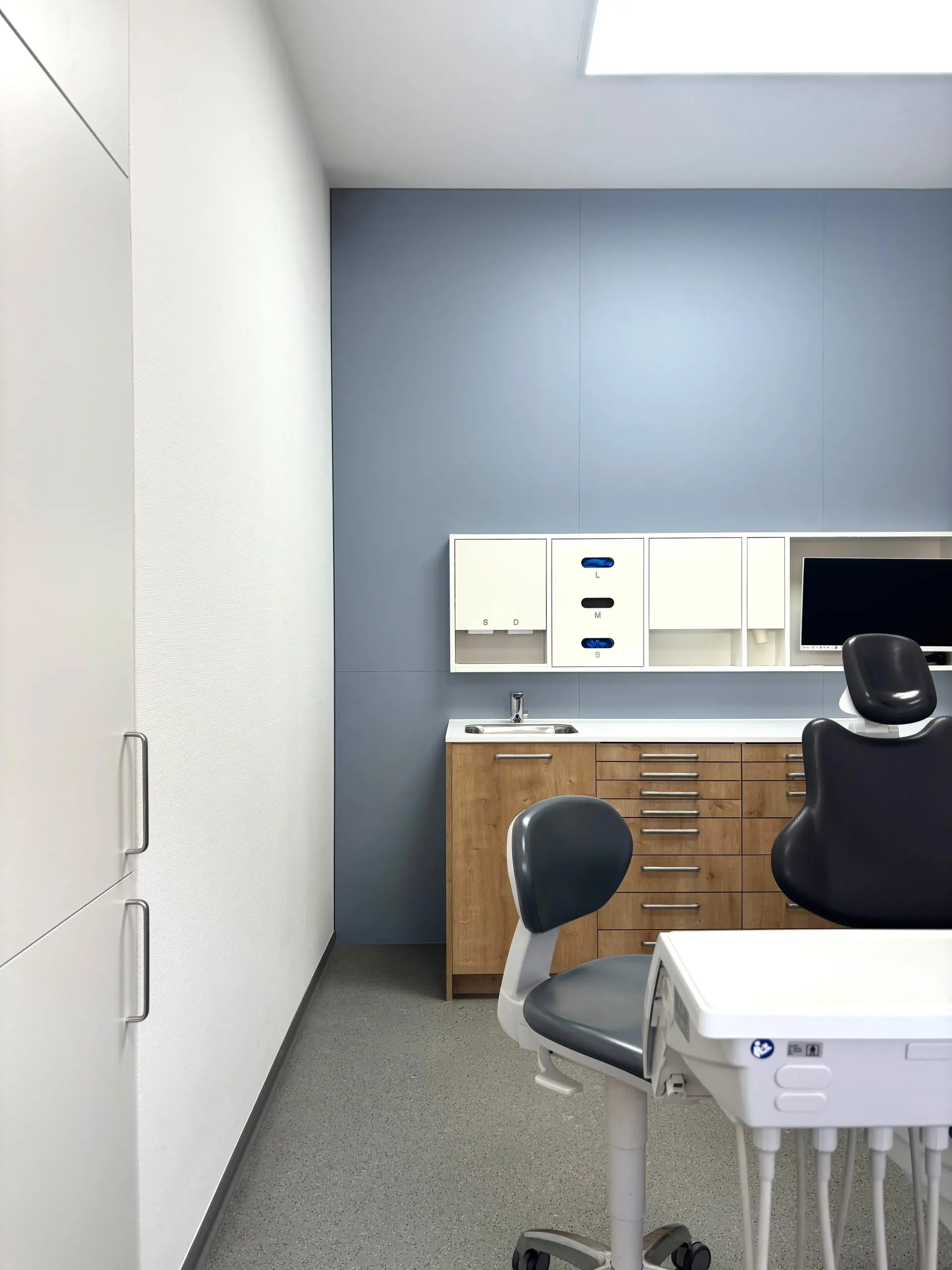 Behandlungsraum mit weißem Einbauschrank, Arbeitsplatz und Bildschirm